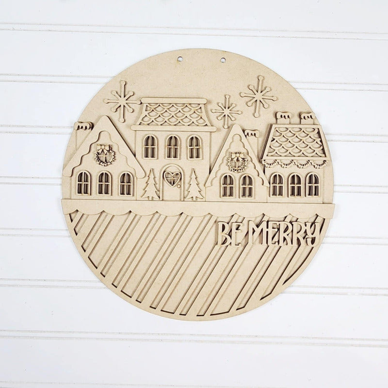Round wooden ornament with house design and 'Be Merry!' text on a white background