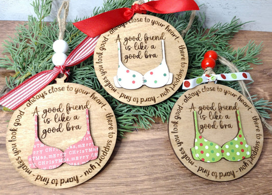 Three wooden ornaments with text 'A good friend is like a good bra' and a bra design, displayed on a holiday decoration branch with red and green ribbons.