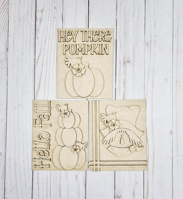 Three wooden cutouts with pumpkin and scarecrow designs on a light wooden background
